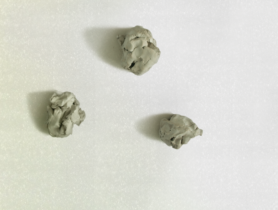 Three small, textured lumps of gray modeling clay on a white surface