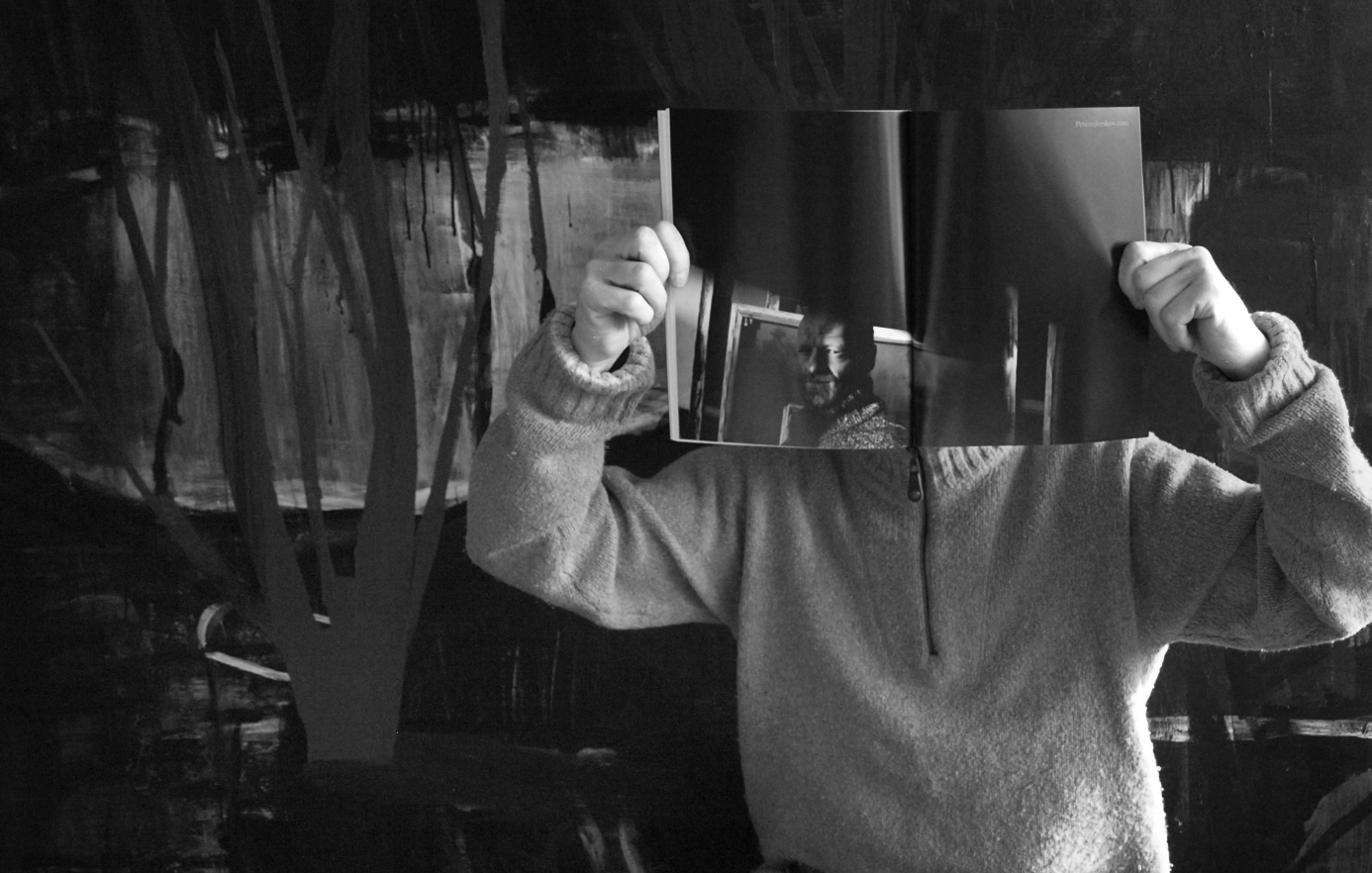 Peter Ejlerskov holder kunst-magasin foran ansigtet i sort-hvidt atelier